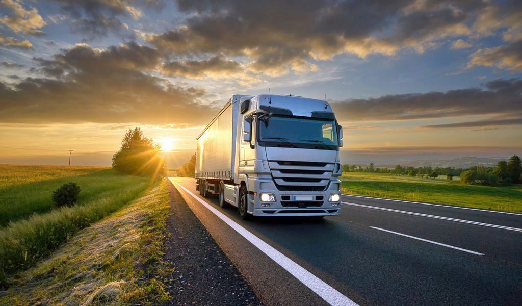 Truck driving on the asphalt road in rural landscape at sunset with dark clouds